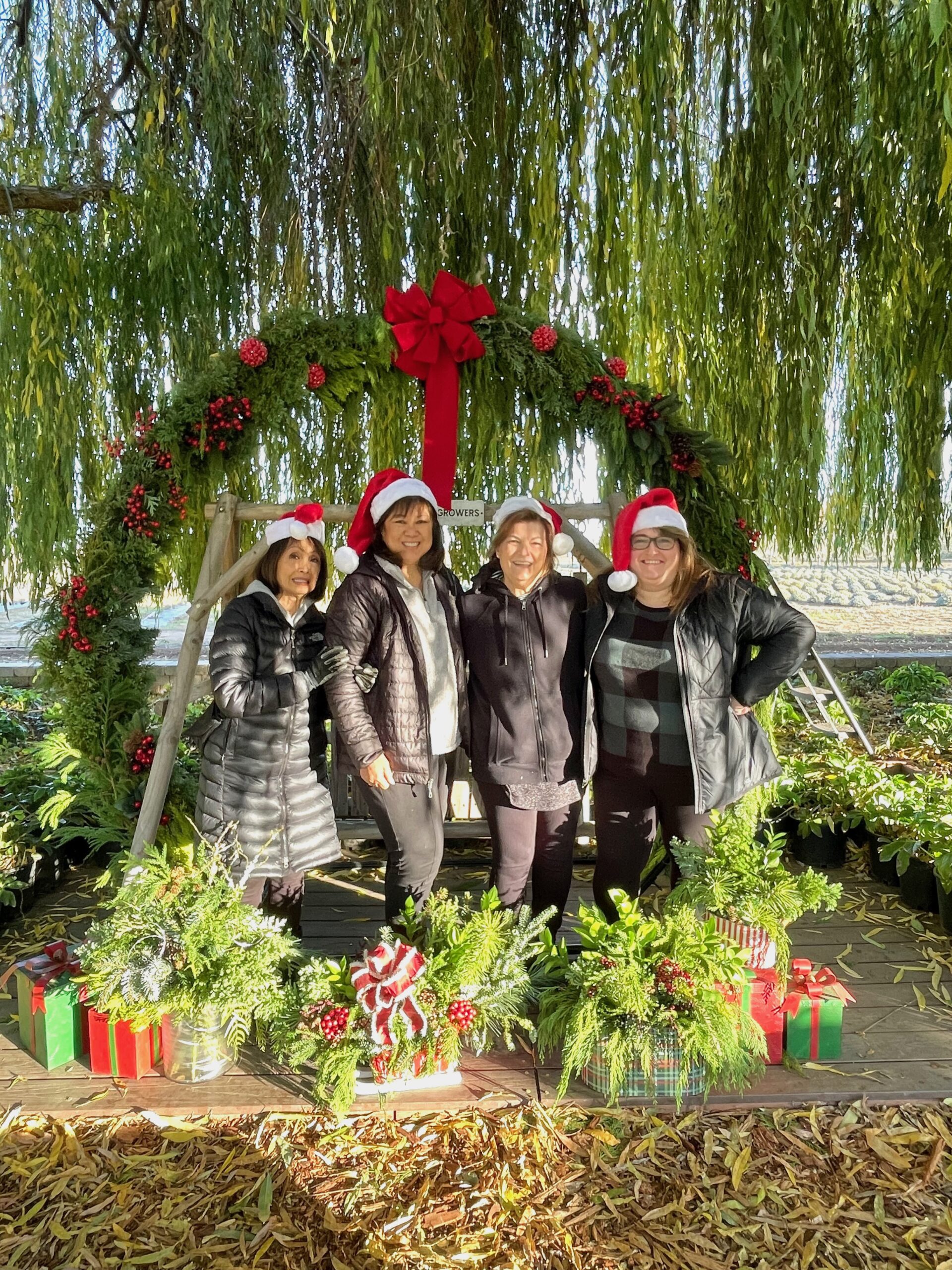 Four ladies standing under big Christmas Wreath at HvH Specialty Growers