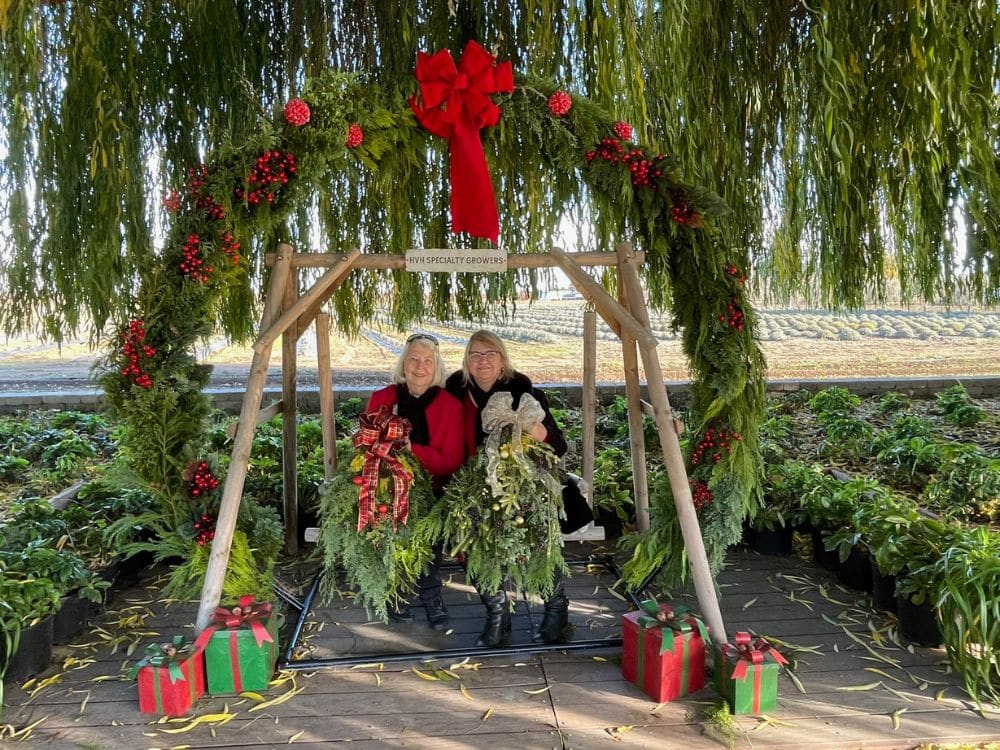 2 women sitting on a swing below the 8 ft. Christmas wreath at HvH Specialty Growers in Fairfield, California