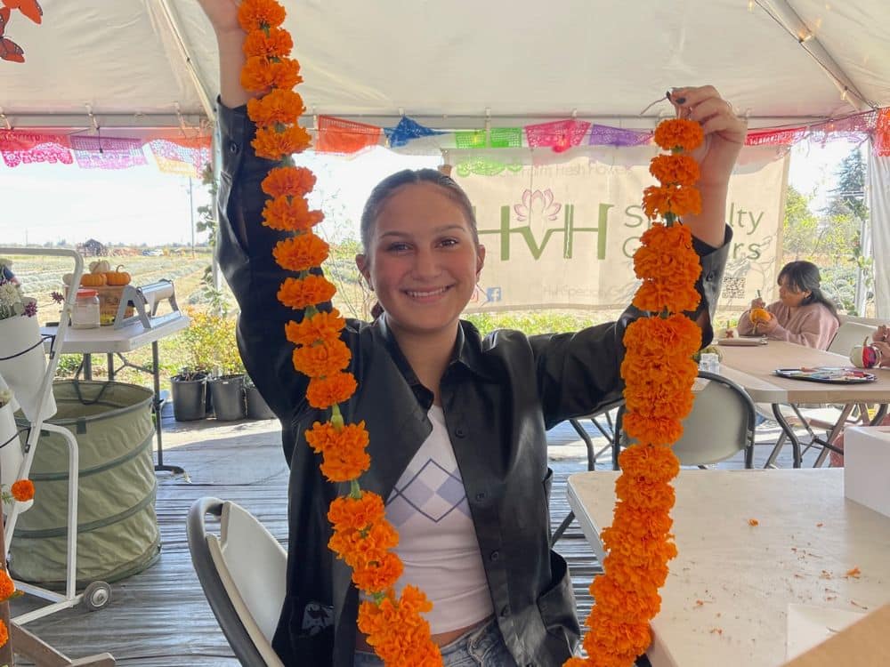 Woman holding the orange marigold garland made with fresh cut marigolds at HvH Specialty Growers in Fairfield, California